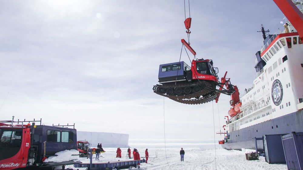 Un PistenBully es levantado por una grúa desde el barco hacia el hielo perpetuo de la Antártida.