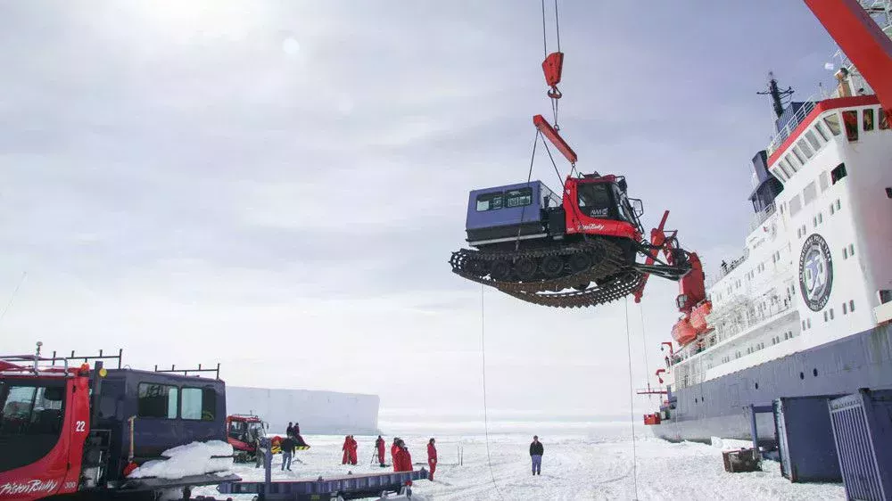 Ein PistenBully wird mit einem Kran vom Schiff auf das ewige Eis der Antarktis gehoben