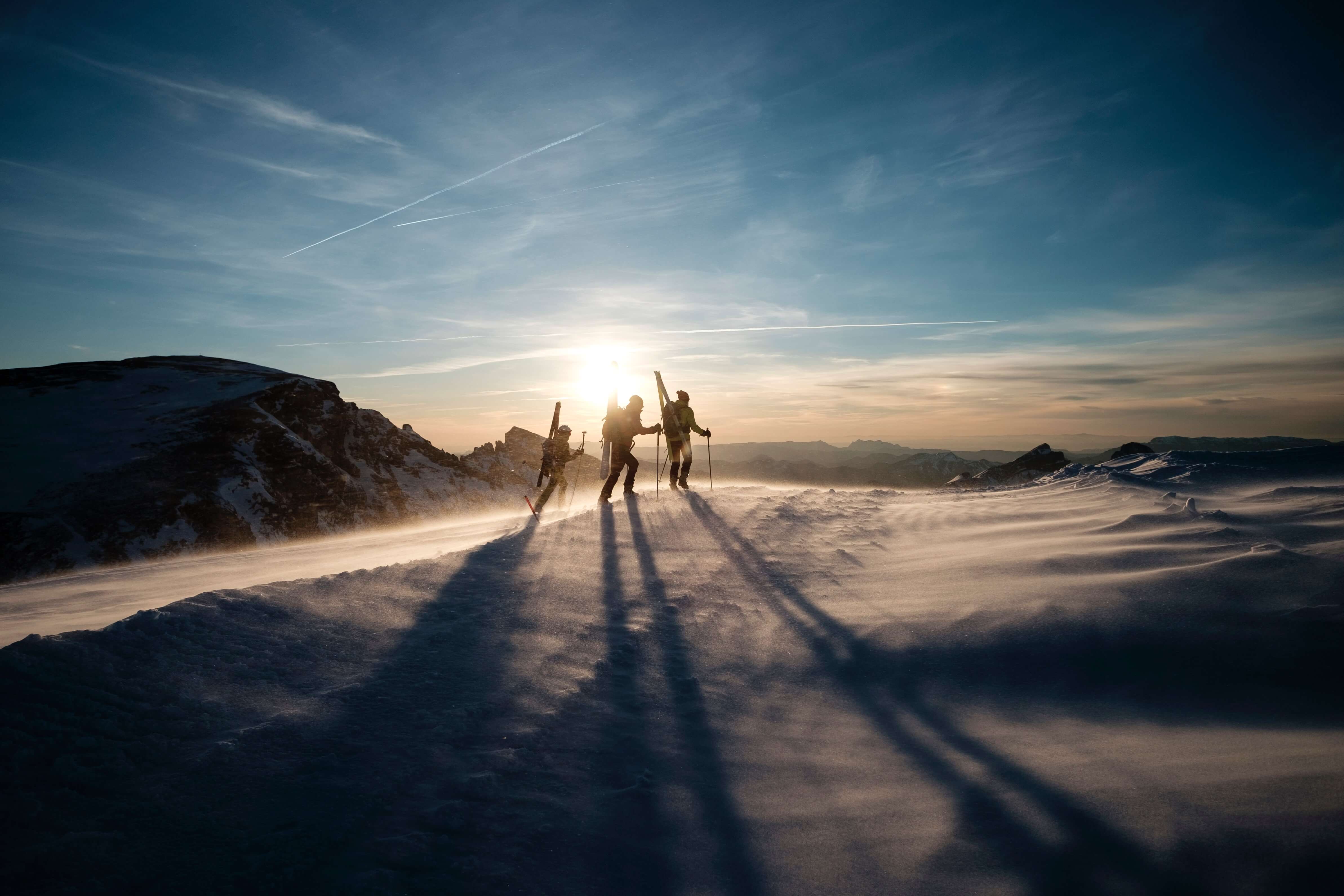 Three mountaineers climb a peak in the morning sun. 